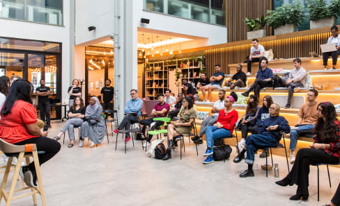 Students seated in a modern atrium, learning from a panel of speakers at BrainStation London.